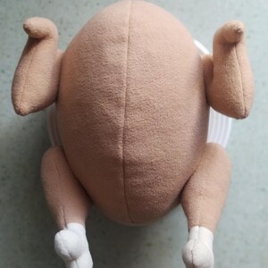 May include: A plush toy shaped like a roasted turkey. The toy is brown with white feet and is made of soft, fuzzy fabric.