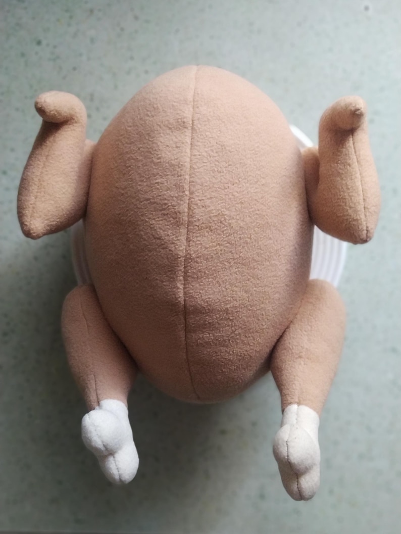 May include: A plush toy shaped like a roasted turkey. The toy is brown with white feet and is made of soft, fuzzy fabric.
