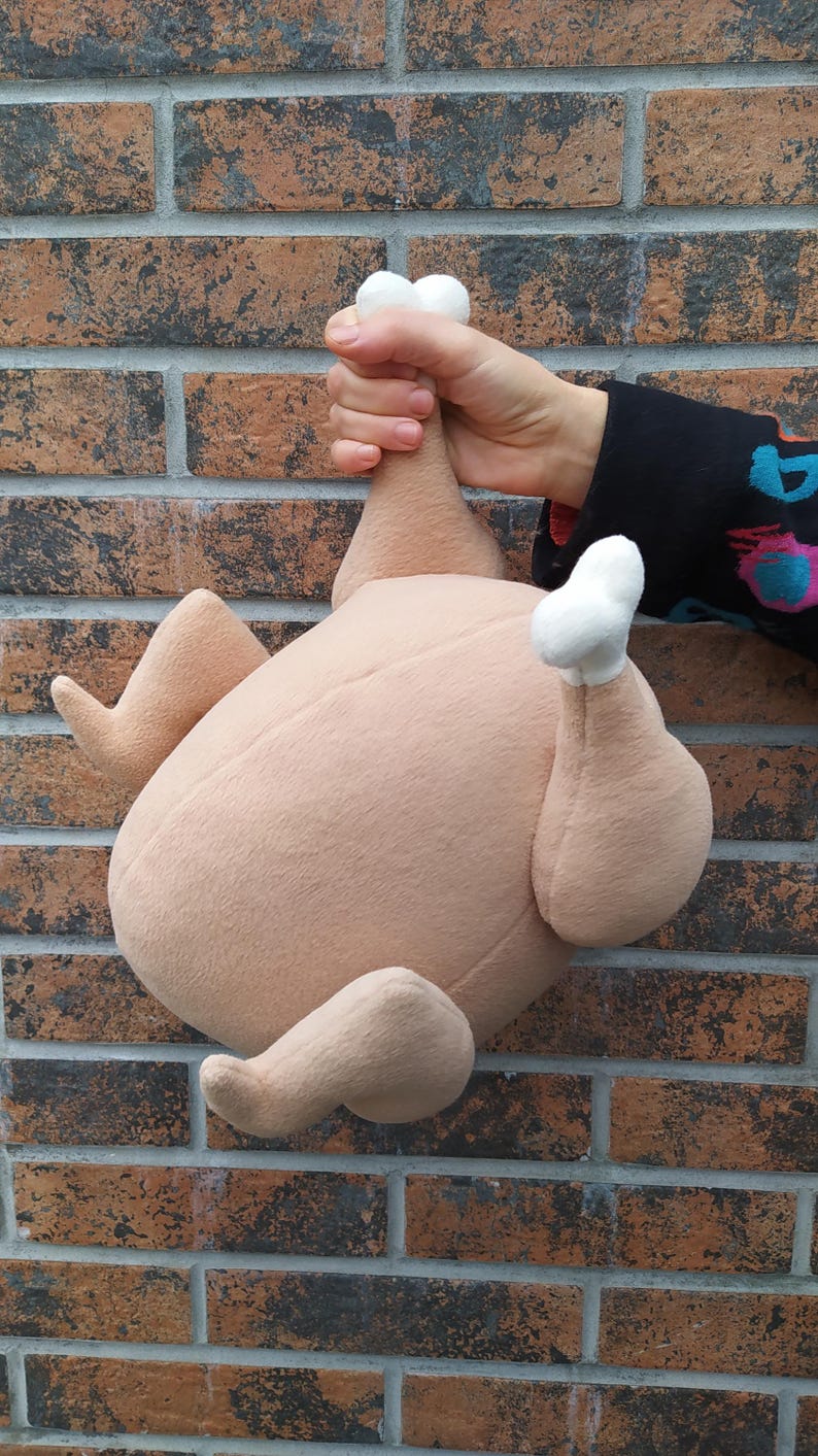 May include: A plush toy shaped like a roast chicken. The chicken is brown and has white feathers on the ends of its wings and legs.