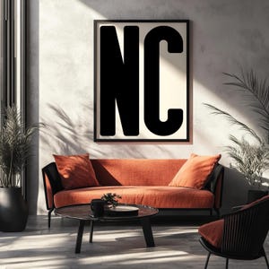 Peut inclure: Un salon moderne avec un canapé orange brûlé et des détails noirs, accompagné de coussins assortis. Au-dessus du canapé, une affiche encadrée en noir affiche les lettres "NC" en gras noir. Une table basse ronde et une chaise noire complètent la scène.