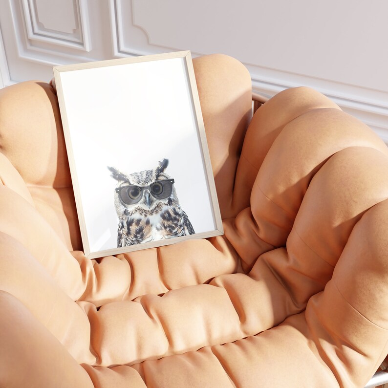 May include: A framed print of an owl wearing sunglasses. The owl is looking directly at the camera. The print is sitting on a light brown, tufted couch.