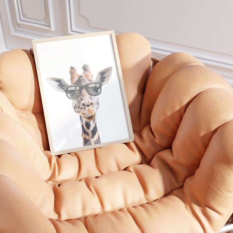 May include: A framed print of a giraffe wearing sunglasses. The giraffe is looking directly at the camera. The print is in a light wood frame and is sitting on a tan leather chair.