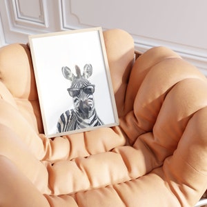 May include: A framed print of a zebra wearing sunglasses. The zebra is looking directly at the camera. The print is sitting on a light brown, tufted couch.