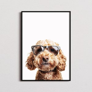 Op de afbeelding: Een ingelijste wandkunstprint met een goudbruine hond met krullend haar die een bril met zwart montuur draagt. De hond is gecentreerd tegen een helderwitte achtergrond, met zijn oren die het gezicht omlijsten en zijn donkere neus zichtbaar onder de bril.
