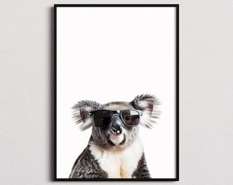 May include: A framed wall art print featuring a koala with grey and white fur wearing black-rimmed sunglasses. The koala is centered against a plain white background, and the entire image is enclosed within a thin, simple black rectangular frame.