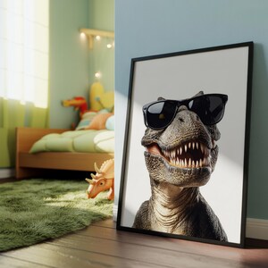 以下が含まれることがあります： 黒いサングラスをかけたティラノサウルスレックスのクローズアップが特徴の額入りプリント。 恐竜は詳細な肌の質感と鋭い歯を持っています。 プリントは黒いフレームに入っており、青い壁に立てかけられています。