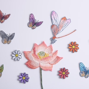 May include: A collection of embroidered iron-on patches featuring a pink lotus flower, butterflies, and daisies. The patches are perfect for adding a touch of whimsy to clothing, bags, or other fabric items.