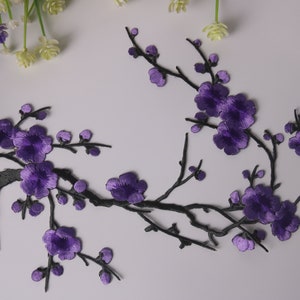 May include: Purple embroidered flower branch applique. The applique features a delicate branch with multiple purple flowers and buds. This design is perfect for adding a touch of elegance to clothing, bags, or home decor projects.