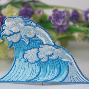 May include: A blue and white embroidered iron-on patch depicting a stylized wave.