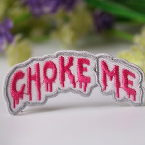 Könnte beinhalten: Weißer Bügel-Patch mit den Worten "CHOKE ME" in pinken, tropfenden Buchstaben.