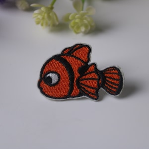 May include: Orange and black embroidered iron-on patch of a cartoon clownfish.