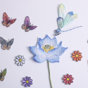 May include: A collection of embroidered iron-on patches featuring a blue lotus flower, a dragonfly, butterflies in various colours, and small flowers.