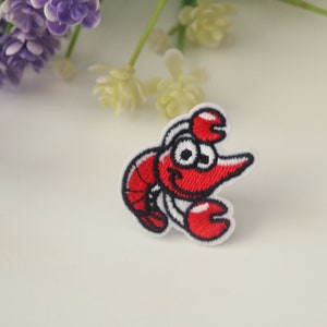 May include: Red embroidered iron-on patch of a cartoon lobster with white eyes and a smile.