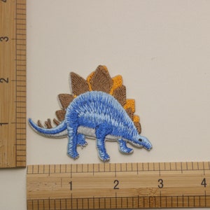 Pu&ograve; includere: Toppa ricamata blu e marrone da stirare a forma di dinosauro con una schiena spinosa.