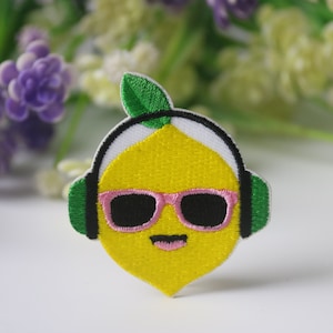 Może przedstawiać: Żółty cytryn z zielonym listkiem na górze, w różowych okularach przeciwsłonecznych i zielonych słuchawkach. Cytryn ma uśmiechniętą twarz.