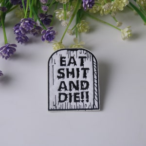 May include: White iron-on patch with black embroidery that reads "Eat Shit and Die!" The patch is shaped like a tombstone.