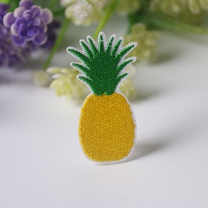 May include: A yellow pineapple with green leaves embroidered on a white fabric patch.