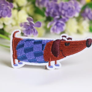 Puede incluir: Parche bordado para planchar de un dachshund marrón con una camisa de cuadros morados y azules.