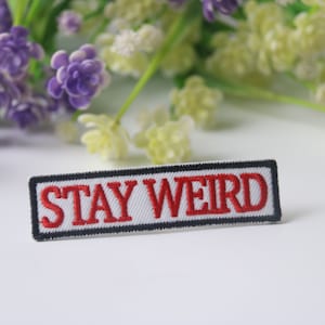May include: White embroidered patch with black trim and red lettering that says "STAY WEIRD".