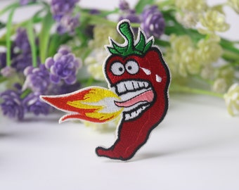 Könnte beinhalten: Gestickter Bügel-Patch mit einer roten Chilischote mit einem Comic-Gesicht, die Feuer aus ihrem Mund bläst. Die Chilischote hat einen grünen Stiel und weiße Zähne.