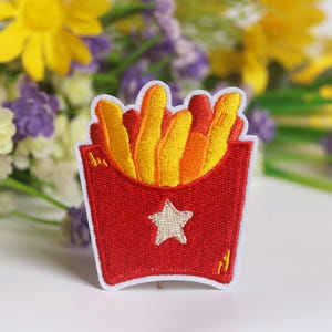 May include: Red and white embroidered iron-on patch of a box of french fries with a white star on the front.
