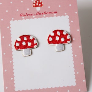 May include: Two red and white mushroom-shaped embroidered patches with white polka dots on a pink card with white polka dots. The card has the text "Gulese Mushroom" on it.