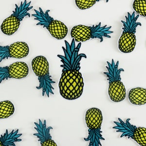 May include: A white background with multiple embroidered pineapple patches in various sizes. The pineapples are yellow with green leaves and blue accents.