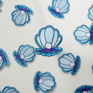 Op de afbeelding: Een verzameling blauwe en paarse geborduurde strijk-op patches met een parel in een schelp.