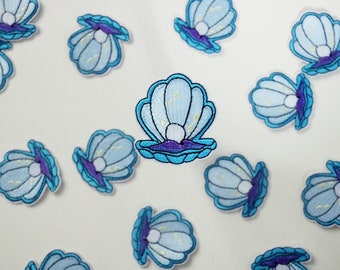 May include: A collection of blue and purple embroidered iron-on patches featuring a pearl inside a seashell.
