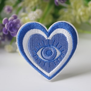 May include: Blue and white embroidered heart-shaped patch with a blue evil eye design.