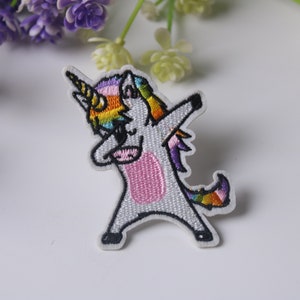 Op de afbeelding: Geborduurde strijkpatch met een wit eenhoorn met een regenboogmanen en -staart, in een dabbing pose.