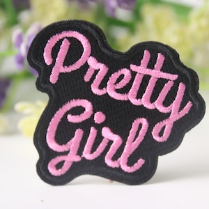 May include: Pink embroidered patch with the text "Pretty Girl" on a black background.