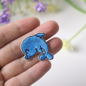 May include: A blue embroidered iron-on patch of a dolphin jumping out of the water.