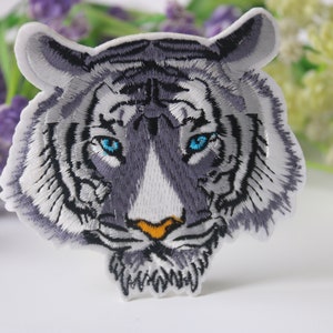 May include: White embroidered iron-on patch of a white tiger's face with blue eyes.