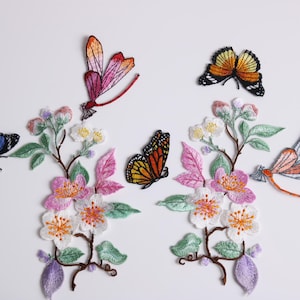 Könnte beinhalten: Gestickte Blumenaufnäher mit Schmetterlingen und Libellen. Die Aufnäher haben rosa, orange, blaue und gelbe Schmetterlinge mit detaillierten Flügeln. Die floralen Elemente umfassen rosa und weiße Blüten, grüne Blätter und lila Akzente.