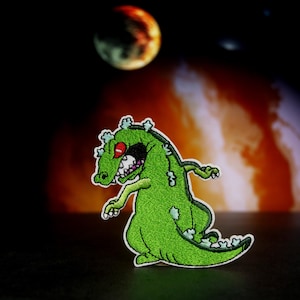 May include: Green cartoon monster with red eyes and a toothy grin. The monster is standing on a red and orange background.