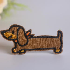 May include: Brown embroidered dachshund dog patch with black outline and yellow and orange accents.