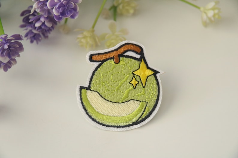 Peut inclure: &Eacute;cusson brod&eacute; repr&eacute;sentant un melon vert avec une tranche coup&eacute;e, r&eacute;v&eacute;lant l'int&eacute;rieur clair. Une tige marron et deux &eacute;toiles jaunes sont au-dessus du melon. L'&eacute;cusson a une bordure blanche.