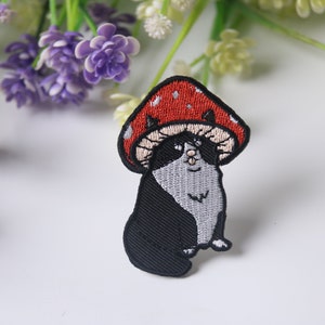 Puede incluir: Parche bordado para planchar de un gato blanco y negro con un sombrero de hongo rojo y blanco.