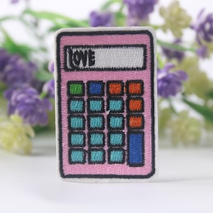 May include: A pink embroidered patch in the shape of a calculator with the word "LOVE" in white. The calculator keys are various colors, including green, blue, and orange. The patch is surrounded by purple and yellow flowers.