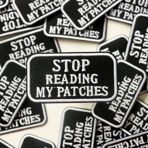 Może przedstawiać: Zbliżenie na kilka czarno-białych haftowanych naszywek z napisem "Stop Reading My Patches".