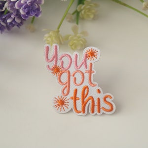 May include: White iron-on patch with pink and orange embroidery that reads "You got this" with small orange starbursts around the text.