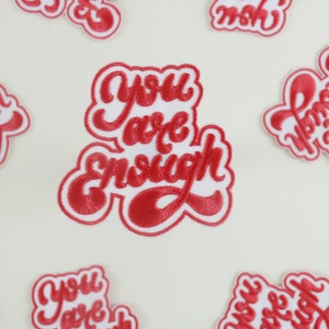 以下が含まれることがあります： 白い背景に「You are enough」という文字が書かれた赤い刺繍のパッチが複数ある