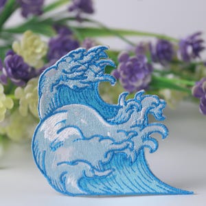 May include: Blue embroidered iron-on patch depicting a stylized wave, perfect for adding a nautical touch to clothing or accessories.