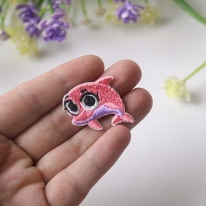 May include: Pink and purple embroidered dolphin patch with large eyes.
