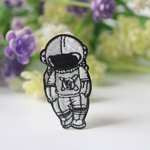 May include: Black and white embroidered iron-on patch of an astronaut in a space suit.