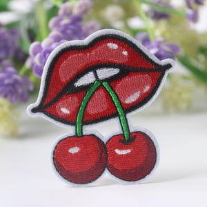 Könnte beinhalten: Roter gestickter Aufnäher mit einem Paar Lippen, die in zwei rote Kirschen mit grünen Stielen beißen.