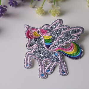 May include: A silver glitter unicorn with a rainbow mane and tail. The unicorn has pink wings and is embroidered with colourful thread.