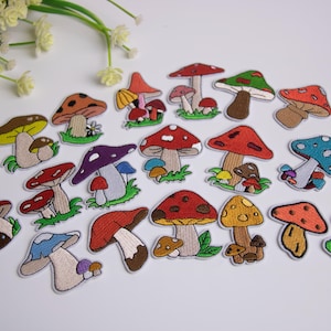 May include: A collection of embroidered mushroom patches in various colors, including red, brown, yellow, and blue. Each patch features a unique mushroom design with detailed stitching and is set against a white background. Some patches include small flowers.