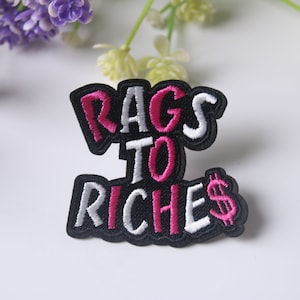 May include: Black iron-on patch with white and pink embroidered text that reads "RAGS TO RICHES" with a pink dollar sign.